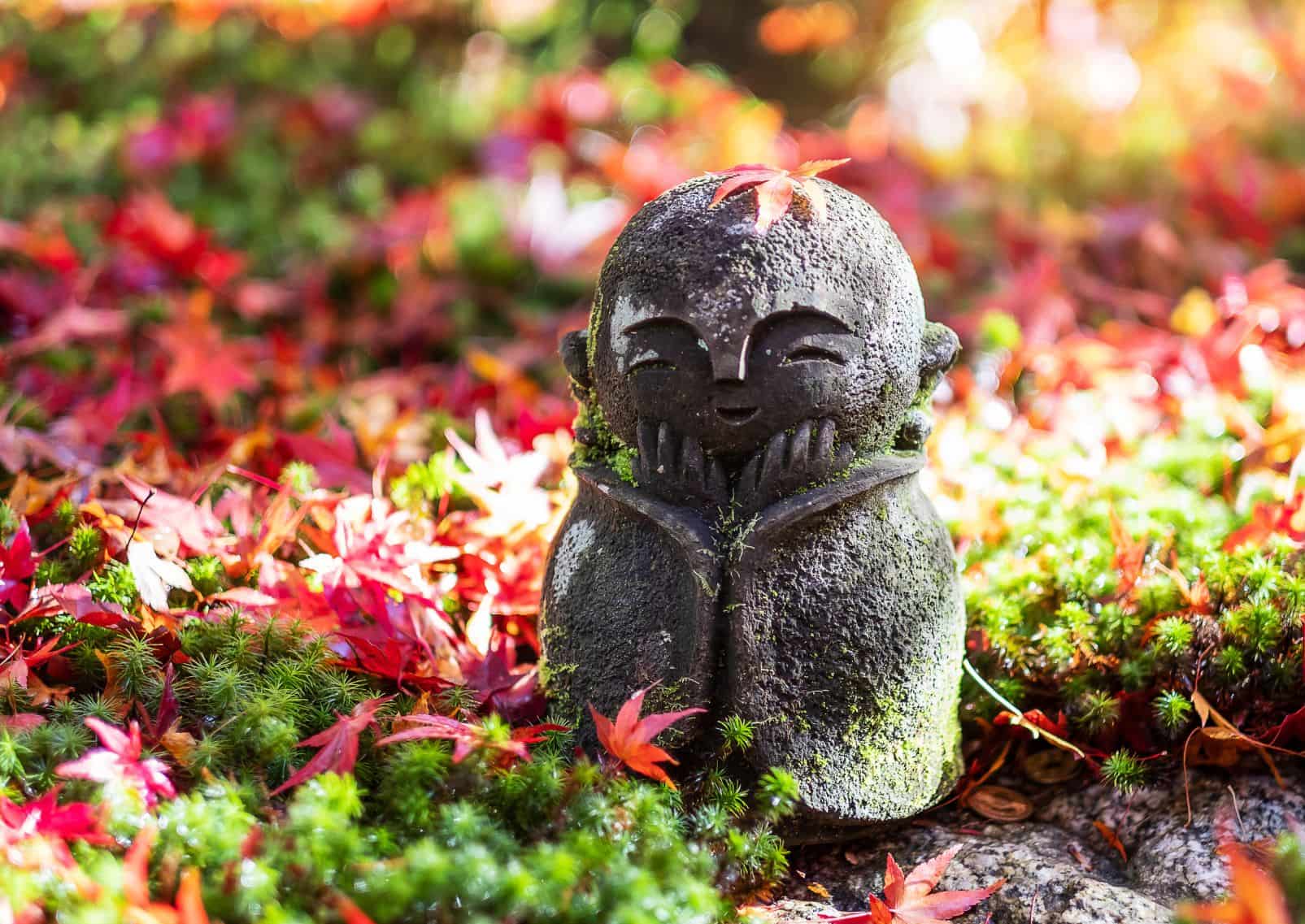 En Jizō-skulptur i dockform fångad i ett ögonblick av stillhet, medan ett rött lönnlöv sakta faller i den japanska trädgården vid Enkōji-templet i Kyoto.