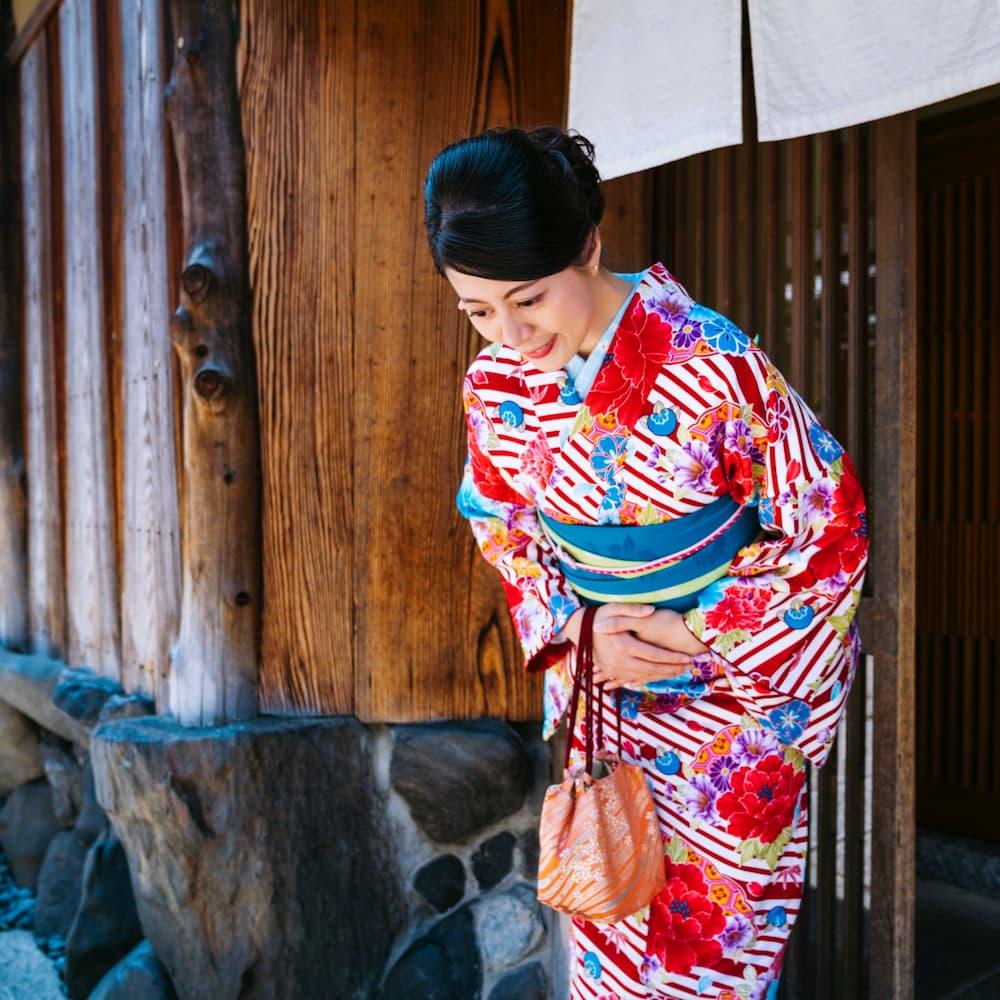 Japansk kvinna i färgglad kimono bugar framför en traditionell träbyggnad i Kyoto