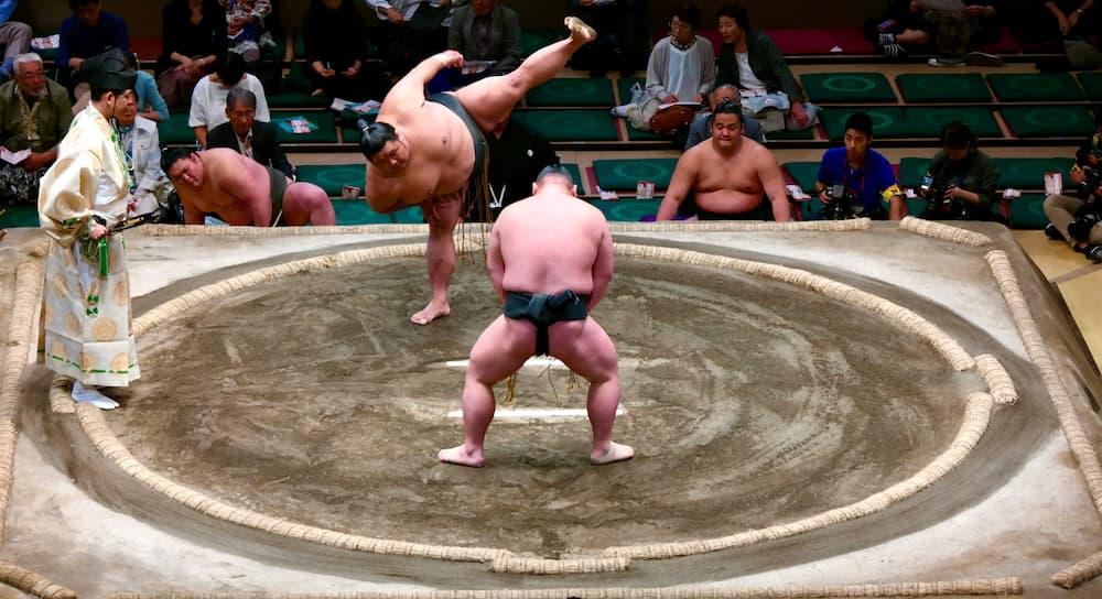 Japanska sumobrottare förbereder sig för en match i ringen, iklädda traditionell mawashi