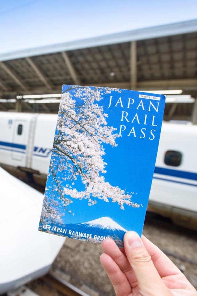 Hand som håller i en Japan Rail Pass-biljett framför en Shinkansen på Tokyo Station
