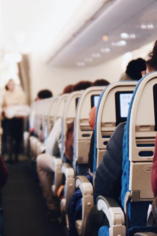 Interiör i ett stort passagerarflygplan med sittande människor och en flygvärdinna i uniform som går längs gången
