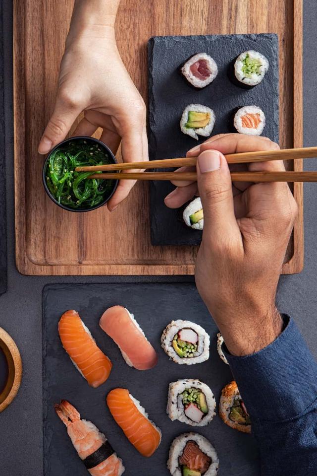 Olika sorters sushi, inklusive nigiri, sashimi och rullar, som delas och äts med ätpinnar