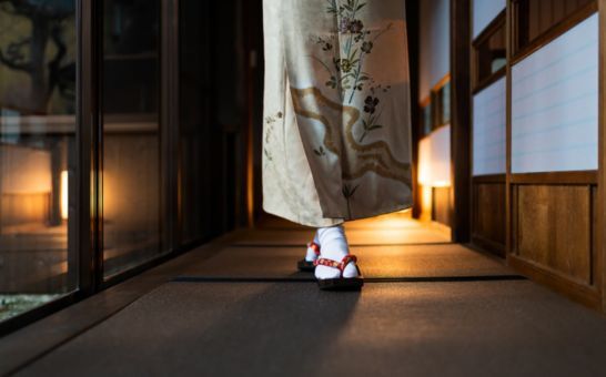 Kvinna i kimono går genom ett traditionellt ryokan med tatamimattor och shoji-dörrar