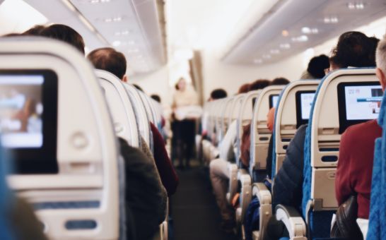 Interiör i ett stort passagerarflygplan med sittande människor och en flygvärdinna i uniform som går längs gången