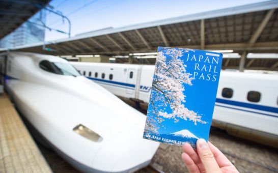 Hand som håller i en Japan Rail Pass-biljett framför en Shinkansen på Tokyo Station