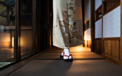 Kvinna i kimono går genom ett traditionellt ryokan med tatamimattor och shoji-dörrar